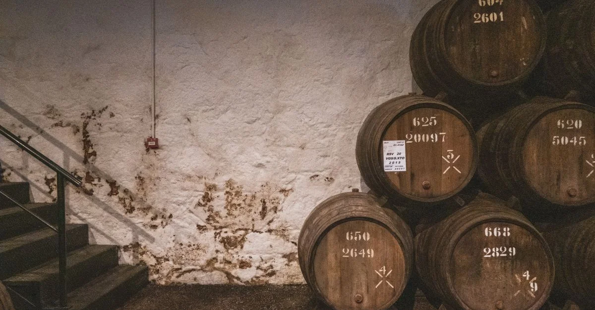 Une pile de fûts en bois vieilli dans une cave de distillerie rustique avec des murs en pierre et des escaliers.
