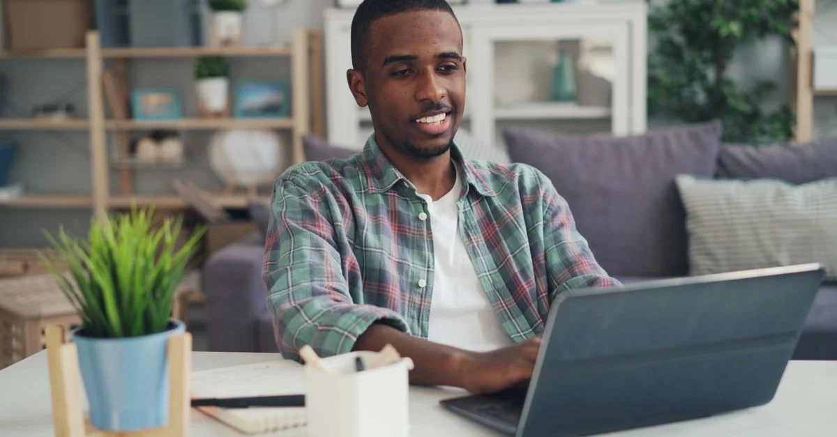 Jeune homme souriant en utilisant un ordinateur portable dans un bureau moderne.