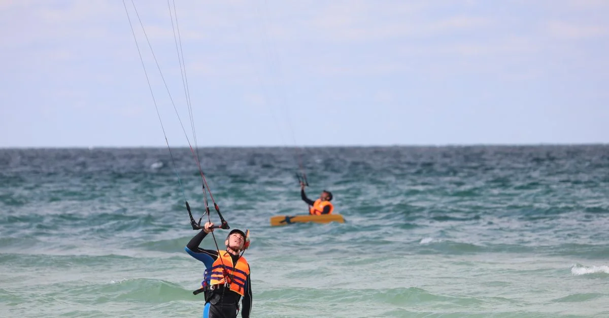 Deux kitesurfeurs en action, profitant de ce sport nautique passionnant en mer ouverte sous un ciel bleu clair.