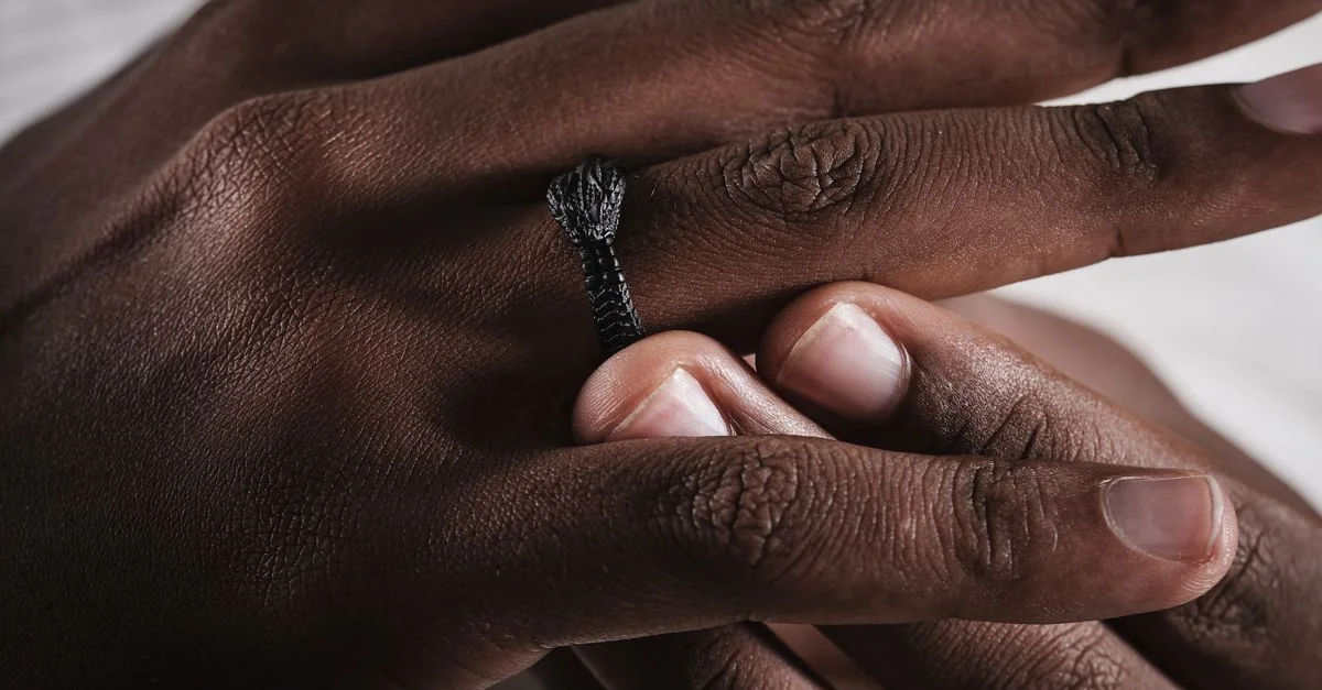 Gros plan d'une bague serpent artisanale sur le doigt d'un homme, mettant en valeur un savoir-faire détaillé.