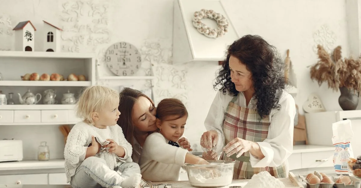 Trois générations cuisinant ensemble dans une cuisine lumineuse, mettant en avant l'amour et la tradition.
