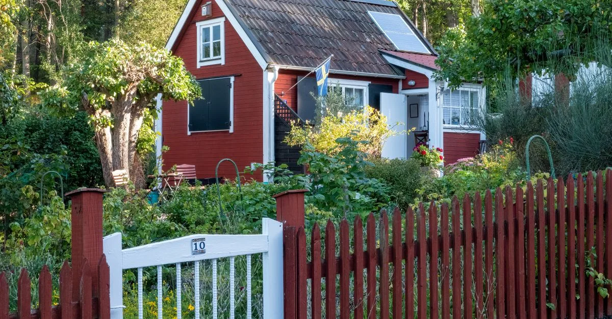 Charmante maison rouge avec un jardin luxuriant, panneaux solaires et drapeau suédois à Stockholm.