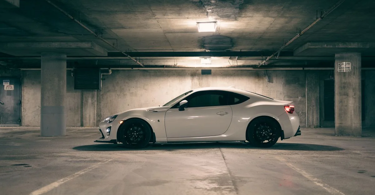 Voiture de sport blanche garée dans un garage souterrain faiblement éclairé, mettant en valeur le design moderne de l'automobile.
