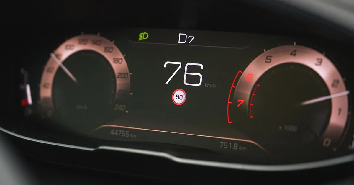 Gros plan sur l'affichage du compteur de vitesse d'une voiture indiquant 76 km/h avec une interface de tableau de bord numérique.